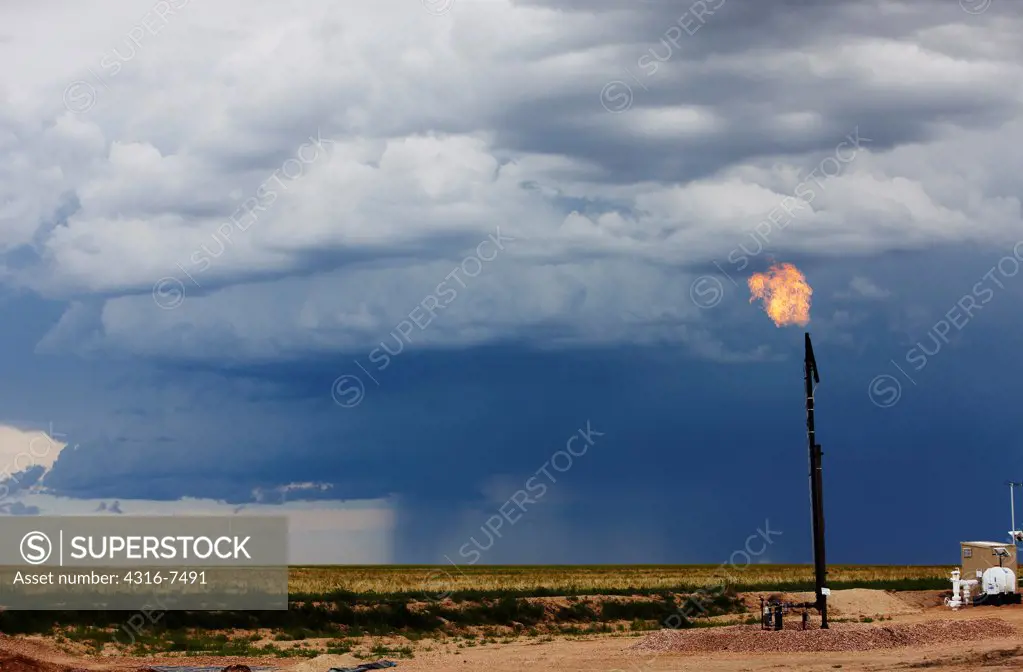 Flare stack at the site of an oil well, with a distant violent thunderstorm during a tornado watch, Colorado
