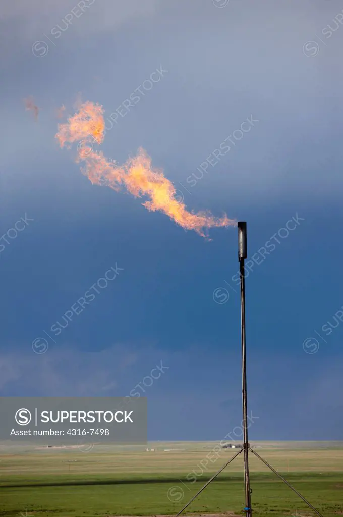 Flare stack at the site of an oil well, with a distant violent thunderstorm during a tornado warning Colorado