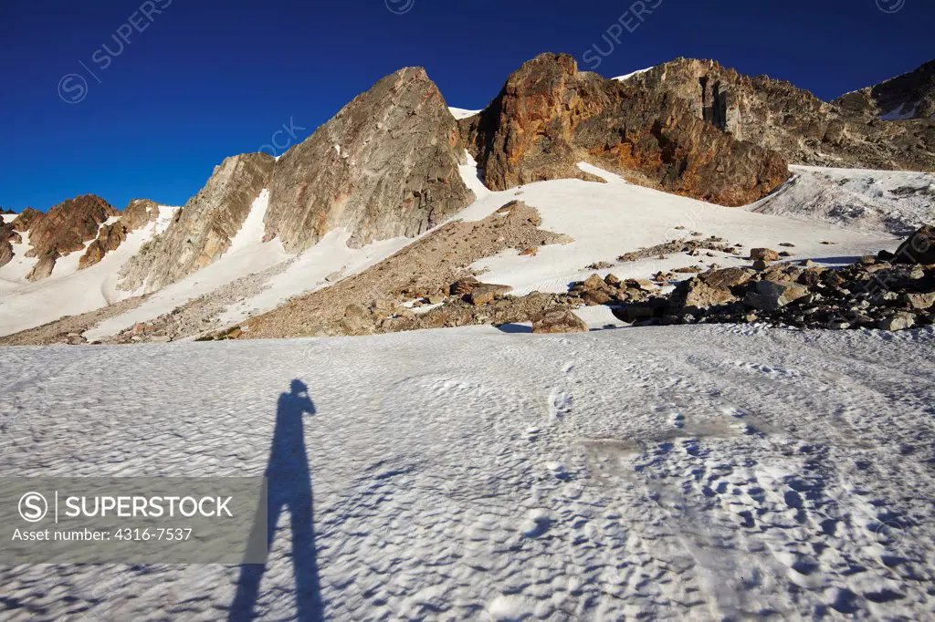 Shadow of photographer on snowfield with steep, soaring mountain peaks of the Snowy Range of the Medicine Bow Mountains of southern Wyoming