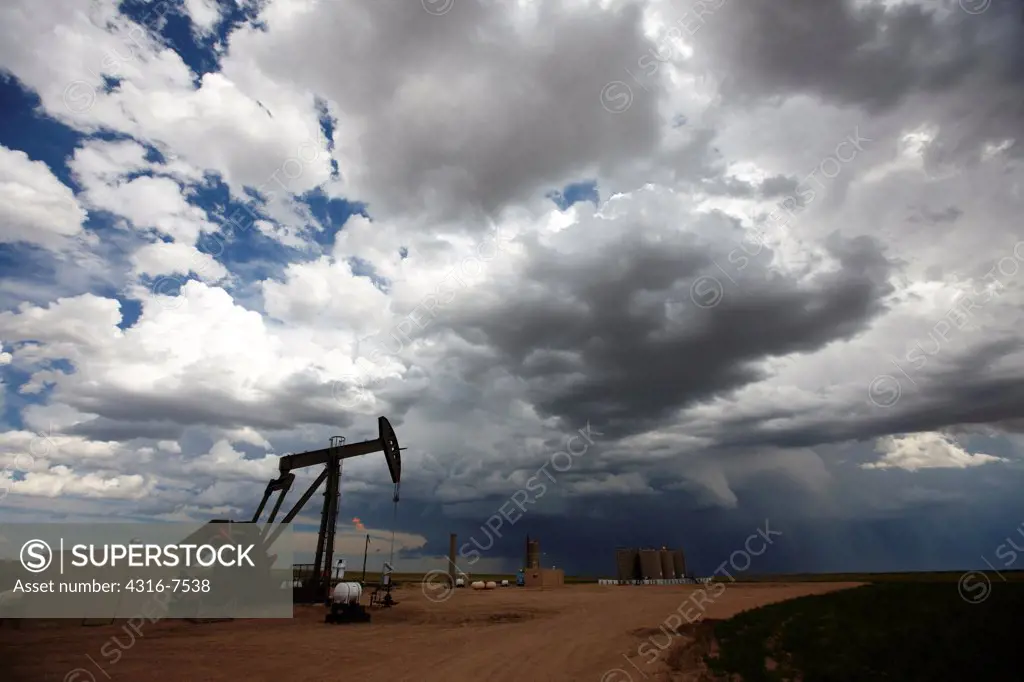 Oil well pump jack, flaring tower, with powerful thunderstorm that produced a funnel cloud, Colorado