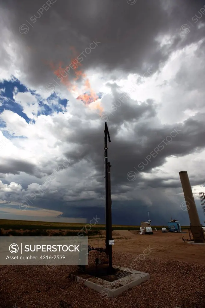 Flare stack at the site of an oil well, with a distant violent thunderstorm during a tornado warning Colorado
