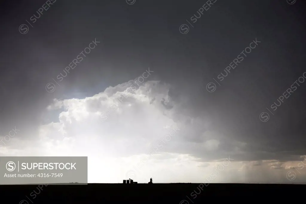 Distant, building thunderstorm, seen through curtains of rain from a powerful thunderstorm that spawned a funnel cloud, oil well pump jack in foreground, Colorado