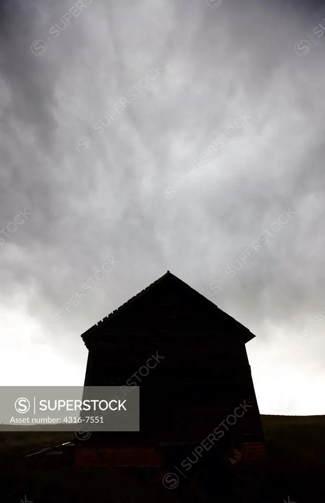 Silhouette of old, Abandoned, decaying, Dustbowl era school house on prairie under a powerful thunderstorm that spawned a funnel cloud, curtains of rain, Colorado