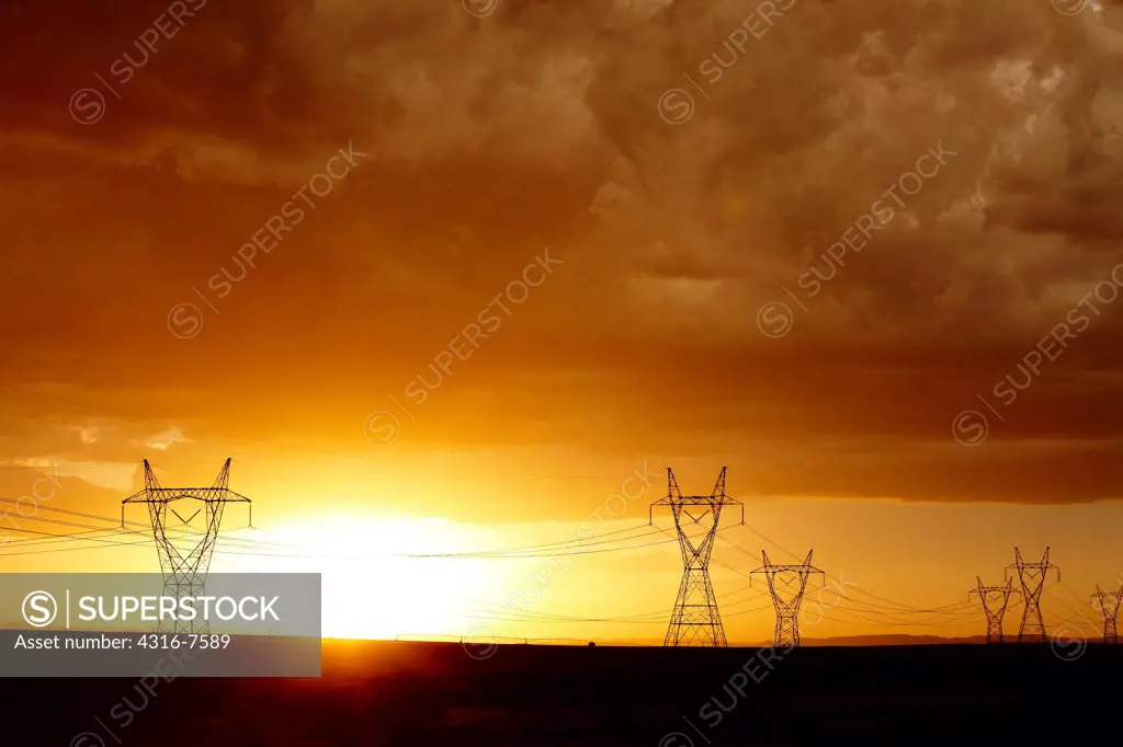 High voltage power lines and transmission towers silhouetted by the setting sun after the passage of a powerful thunderstorm, Colorado