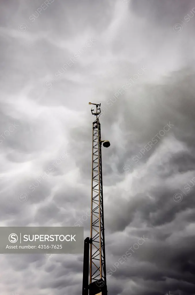 Windmill anemometer atop tower with thunderstorm in distance