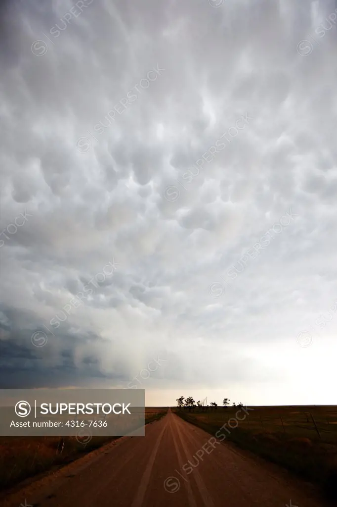 Approaching powerful thunderstorm, with mammatus cloud forms, over empty country dirt road, Colorado