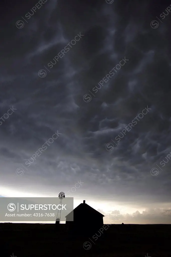 Abandoned ranch house and windmill under a powerful thunderstorm with mammatus clouds, Colorado