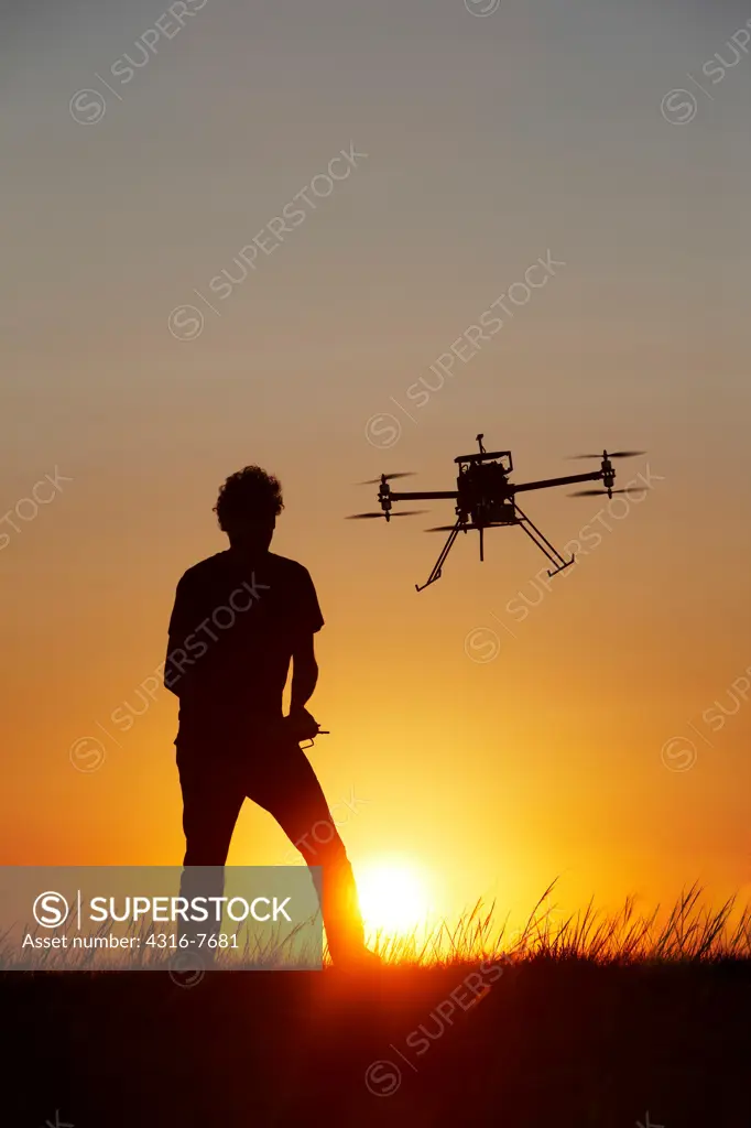 Man flying unmanned aerial vehicle (UAV) or drone, Silhouetted by rising sun, Morning