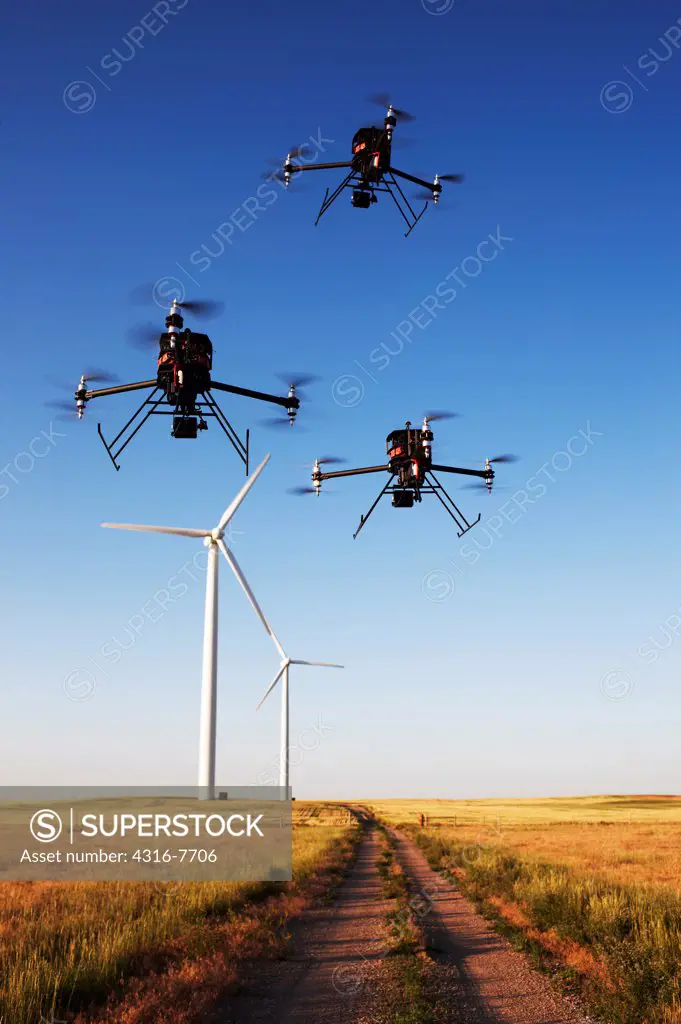 USA, Colorado, Group of three unmanned aerial vehicles (UAVs) or drones, Flying above dirt road, With wind turbines in distance