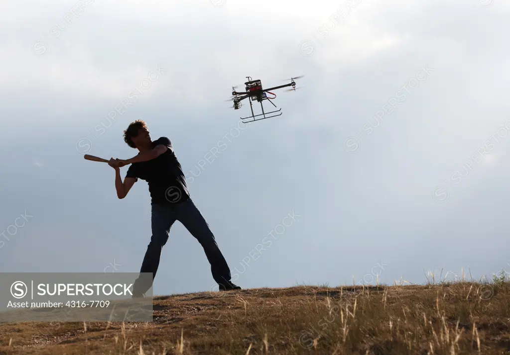 Man winding up to swing bat at unmanned aerial vehicle (UAV) or drone that is invading his privacy or attacking him