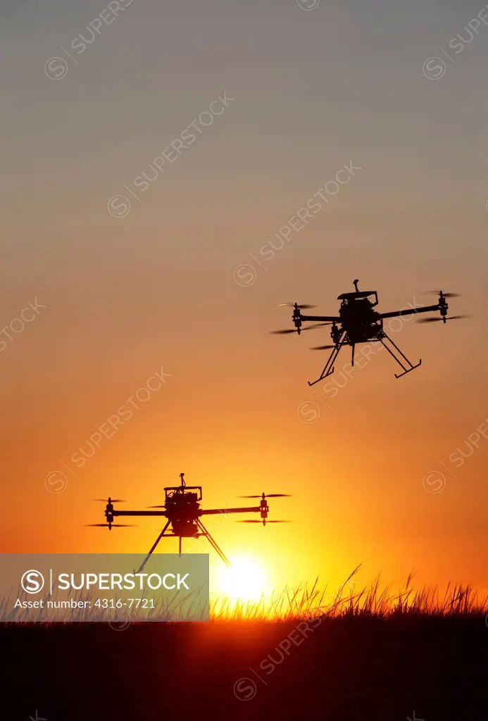 Two unmanned aerial vehicles (UAVs) or drones, In flight, Rising sun, Silhouettes