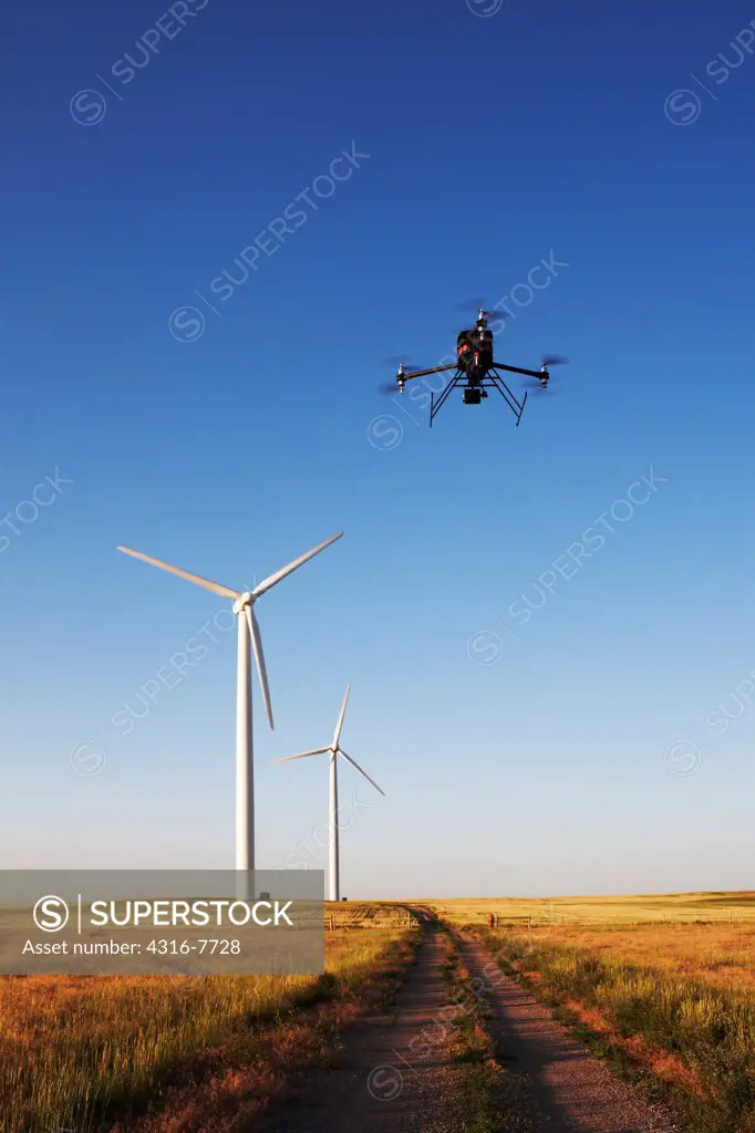 Unmanned aerial vehicle (UAV) or drone flying above empty dirt road with wind turbines in distance
