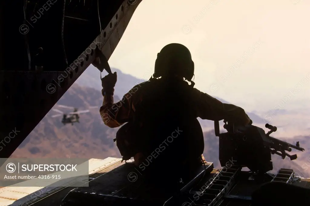 A CH-47 Chinook Ramp Gunner Gazes at His Craft's Sister Helicopter as the Two Roar Through an Eastern Afghan Valley