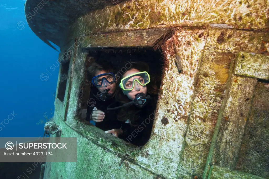 A Pair of Scuba Divers Peer Through a Porthole of the Captain Fox Tugboat Wreck