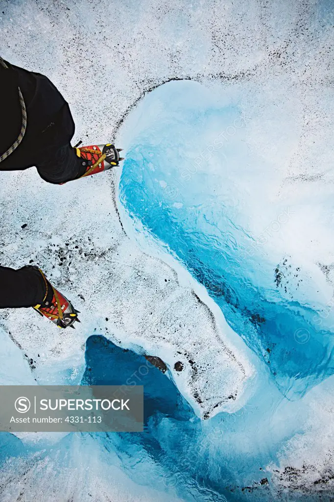 A hiker wearing a pair of crampons walks on top of the Mendenhall Glacier in Juneau, Alaska. The Glacier has many small and large river systems running from within itself.