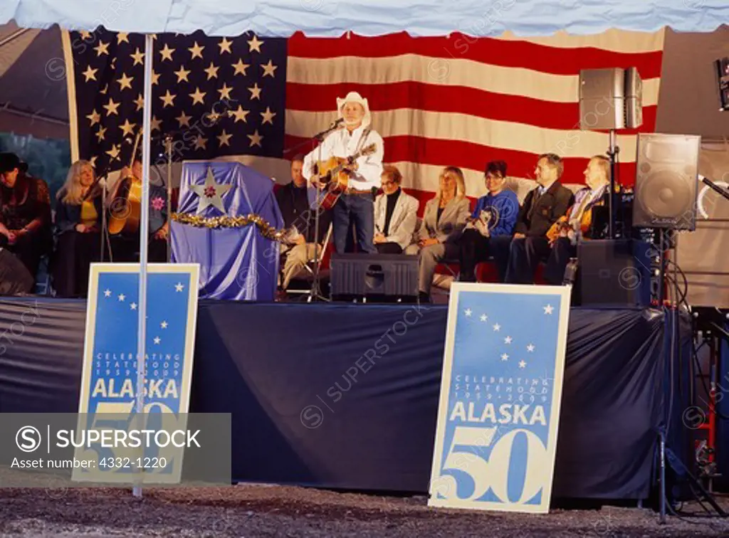 Folk singer Hobo Jim (Jim Varsos) performing at Alaska Statehood 50th Anniversary celebration at Alaska State Fair with Katie Hurley, Governor Sarah Palin (two days before John McCain selected Sarah as his Vice Presidential running mate!), Lt. Governor Sean Parnell and Senator Ted Stevens, Palmer, Alaska.  Rare 49 star flag behind.