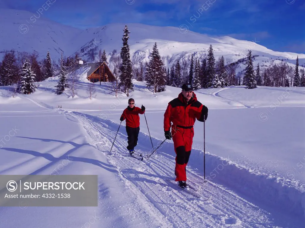Carl Dixon and Blair Aubrey cross-country skiing on Finger Lake with Winterlake Lodge and the Alaska Range beyond, Alaska.