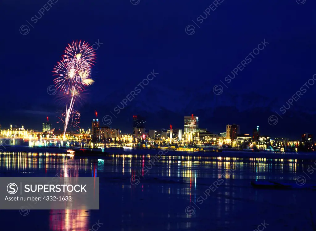 Fur Rondy Celebration fireworks above the skyline of Anchorage with the Chugach Mountains beyond, view from Point MacKenzie, Alaska.