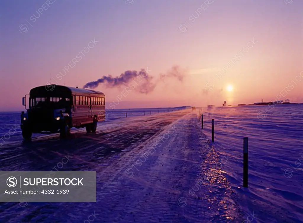 Oil field worker bus on the James Dalton Highway with sun setting over the Deadhorse Airport during 20/20 weather (20 below and 20 knot wind), Arctic Coastal Plain, Alaska.