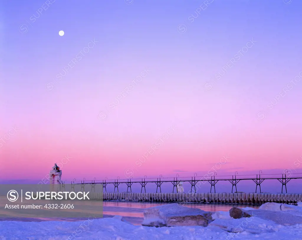 Moon setting at dawn over the South Haven South Pier Lighthouse in winter, entrance of the Black River into Lake Michigan, South Haven, Michigan.