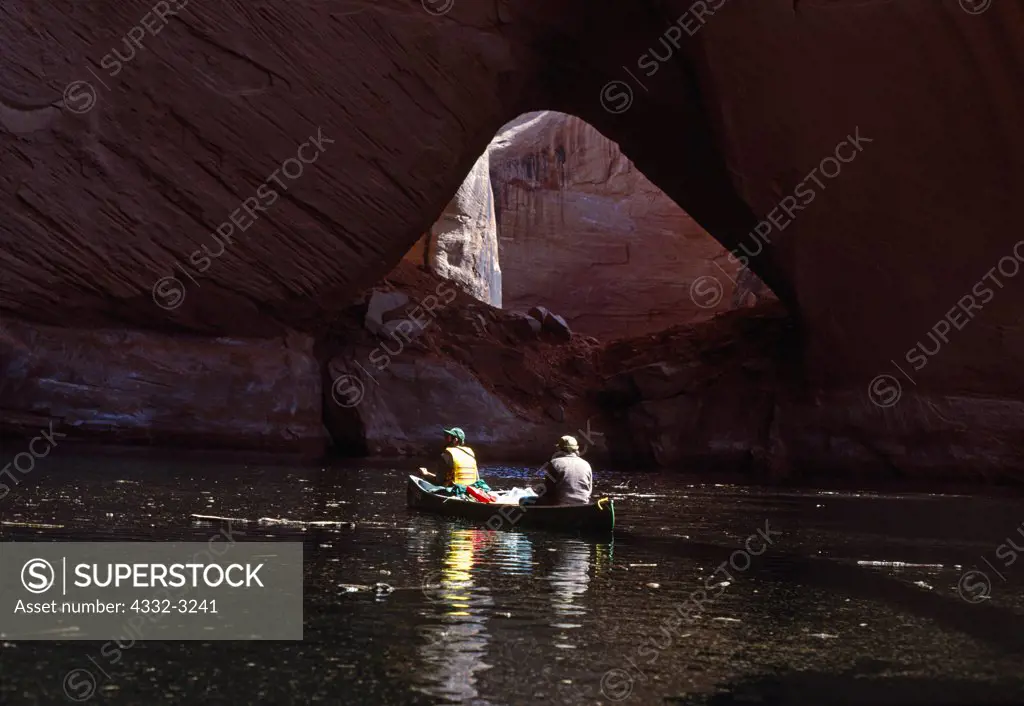 Rick Hutchinson and Jennifer Whipple paddling debris-covered water of Lake Powell in Davis Gulch with La Gorce Arch, Escalante River drainage, Glen Canyon National Recreation Area, Utah.