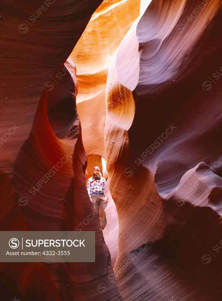 USA, Arizona, Colorado Plateau, Man standing in pothole arch in tortuous groove of slickrock slot canyon