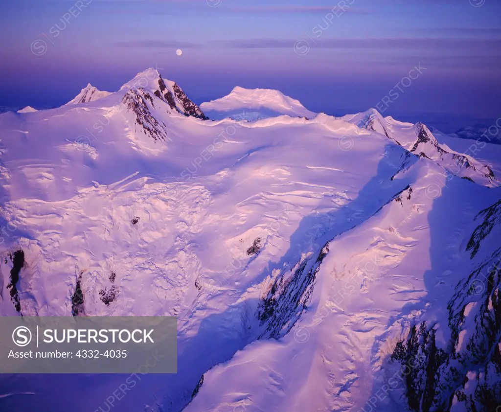 Aerial view of sunset light illuminating Mount Gannett with full moon rising beyond, Chugach Mountains, Alaska.