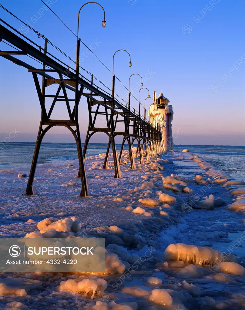Sunrise light illuminating ice-covvered jetty and catwalk leading to the South Haven South Pier Lighthouse, Black River, Lake Michigan, South Haven, Michigan.