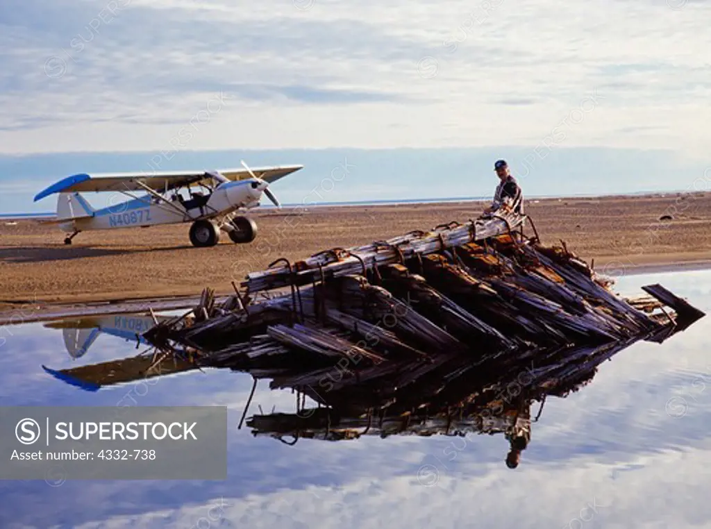 Cape Smythe Air pilot Glenn Hittson inspecting century old wreck of whaling ship on spit of Point Franklin north of Peard Bay, Arctic Ocean, Piper PA18 Super Cub on beach beyond, Alaska.