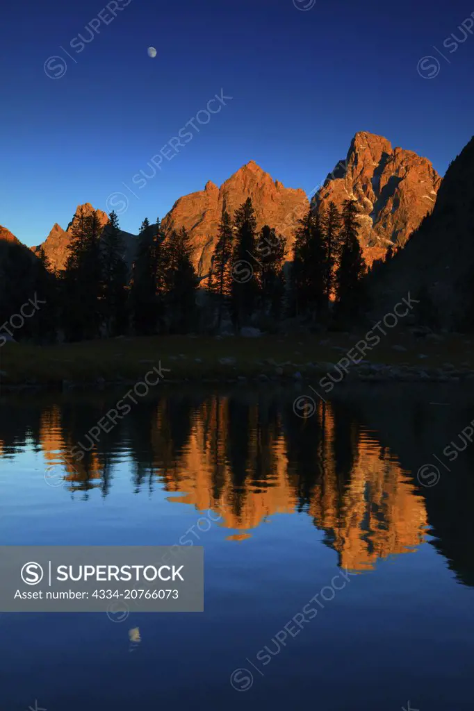 Evening Glow Sunset Light on The Grand Tetons Reflected in Lake Solitude With the Moon From the Back Country of Grand Teton National Park in Wyoming