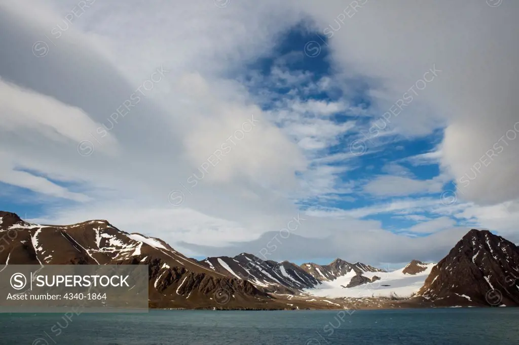 Clouds stretch over a rugged glacial landscape in St. Jonsfjord, west coast of Svalbard, Norway, in summertime.