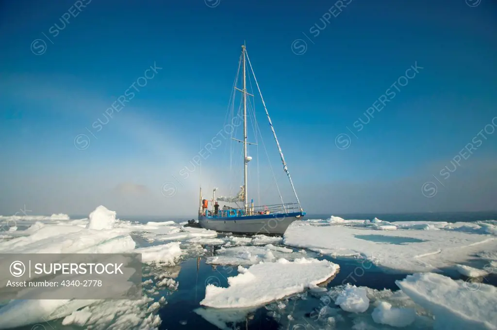 expedition sailing yacht motors through sea ice with an ice rainbow in the distance, Spitsbergen, Svalbard Archipelago, Norway, Summer