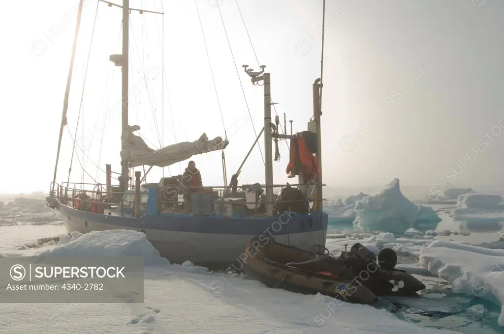 Woman on deck above an expedition sailboat, pulling a zodiac, as it motors through sea ice, off Spitsbergen and the Svalbard Archipelago, Norway, Summer
