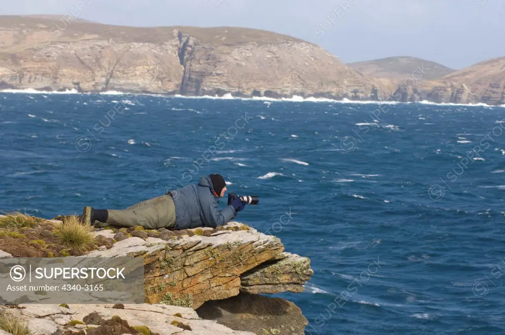 Falkland Islands, Beaver Island, Photographer lying down at water's edge with camera