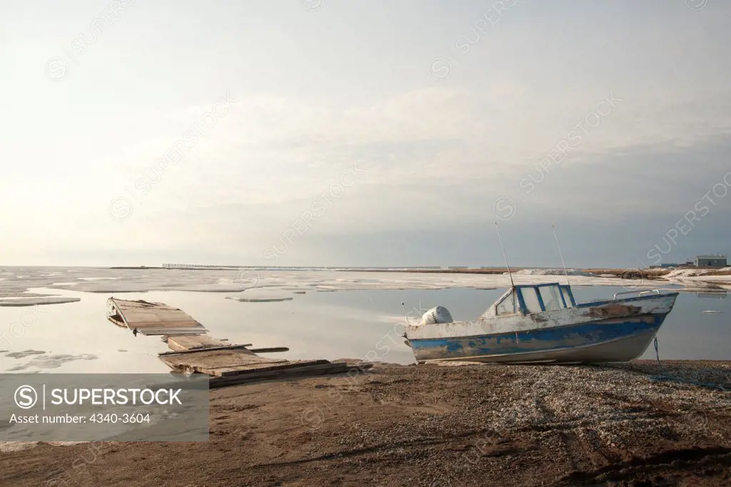 USA, Alaska, North Slope, Barter Island, Brooks Range in distance, Boat parked along Arctic village of Kaktovik with summer sea ice along shore