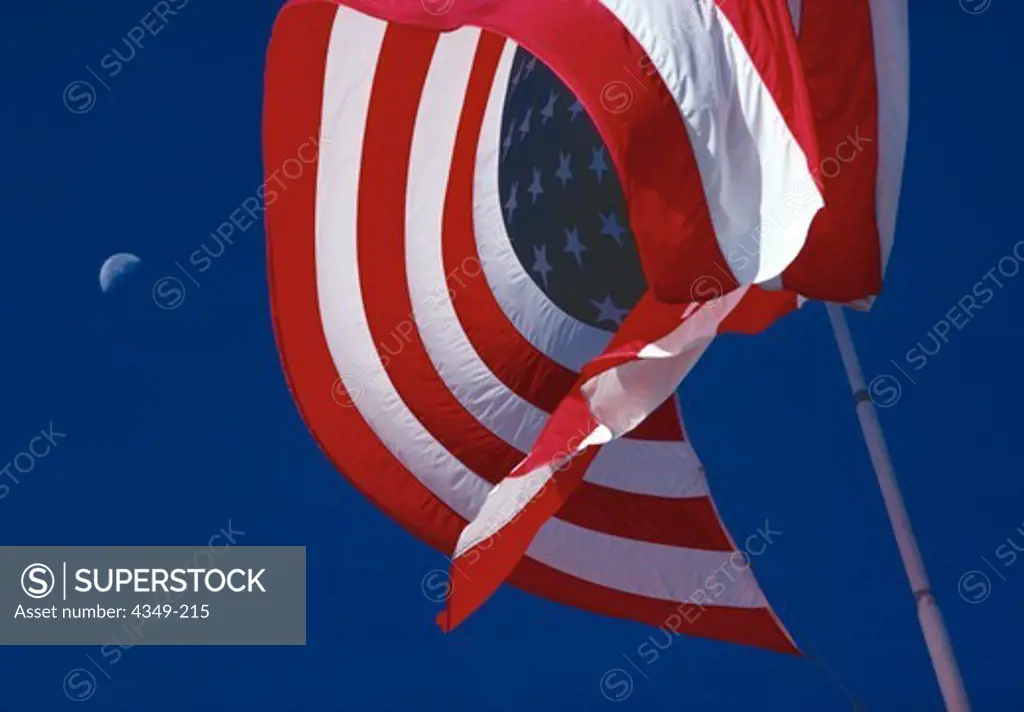 American flag against blue sky with half moon visible