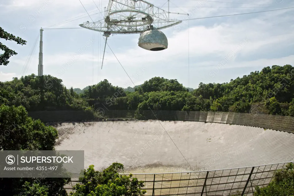 The Arecibo Observatory is a radio telescope just over 1,000 feet (305 m) across, the largest single radio telescope. The main metal collecting dish sits fixed a hemispherical karst sinkhole. Because it is fixed, a spherical reflector hangs 500 feet (150 m) over the dish on a 900 ton platform, known as 'the feed'. The observatory is the primary location of the National Astronomy and Ionosphere Center, NAIC.