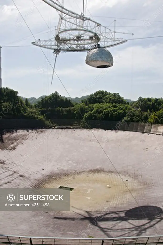 The Arecibo Observatory is a radio telescope just over 1,000 feet (305 m) across, the largest single radio telescope. The main metal collecting dish sits fixed a hemispherical karst sinkhole. Because it is fixed, a spherical reflector hangs 500 feet (150 m) over the dish on a 900 ton platform, known as 'the feed'. The observatory is the primary location of the National Astronomy and Ionosphere Center, NAIC.