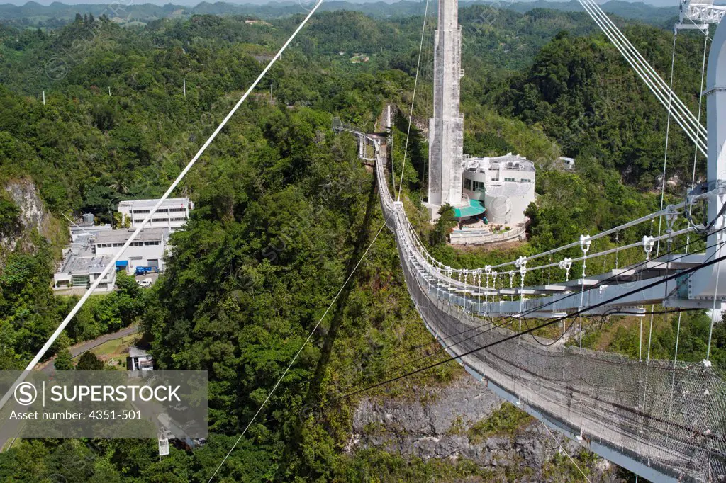 The Arecibo Observatory is a radio telescope just over 1,000 feet (305 m) across, the largest single radio telescope. The main metal collecting dish sits fixed a hemispherical karst sinkhole. Because it is fixed, a spherical reflector hangs 500 feet (150 m) over the dish on a 900 ton platform, known as 'the feed', which can be reached by this hanging stairway. The control center in on the left. The observatory is the primary location of the National Astronomy and Ionosphere Center, NAIC.