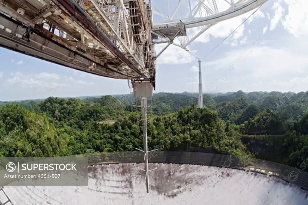 The Arecibo Observatory is a radio telescope just over 1,000 feet (305 m) across, the largest single radio telescope. The main metal collecting dish sits fixed a hemispherical karst sinkhole. In addtion to being a radio telescope, the dish is also a powerful radar transmitter, and has been very useful in radar astronomy in our solar system. This transmitter is on a 900 ton platform known as 'the feed' hanging 500 feet (150 m) over the dish. The observatory is the primary location of the National
