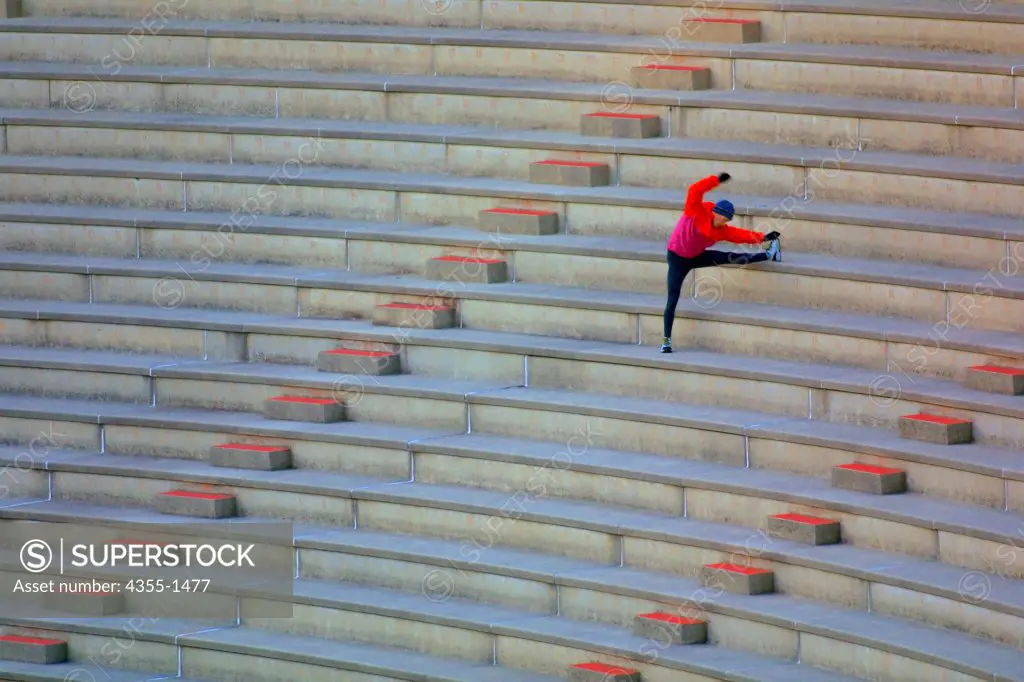 An athlete stretching in the bleachers of a stadium, preparing to run up and down the steps.