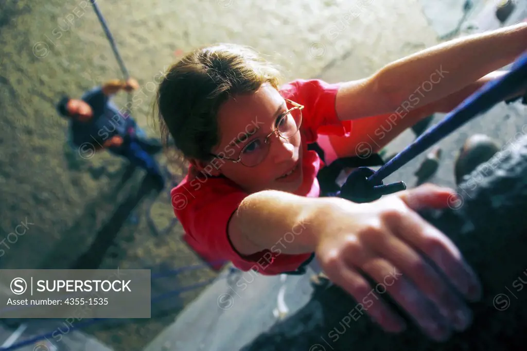 A girl scales an indoor rock climbing wall, with father helping below.