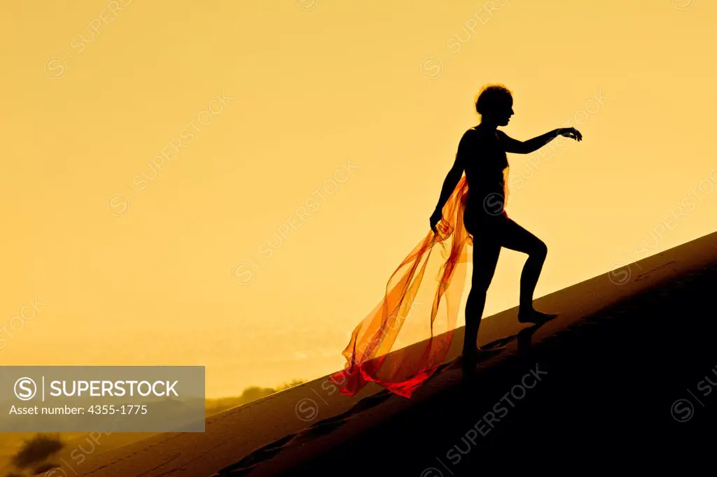 A woman wrapped in red gauzy fabric on the 130 foot tall sand dunes in Mendocino.