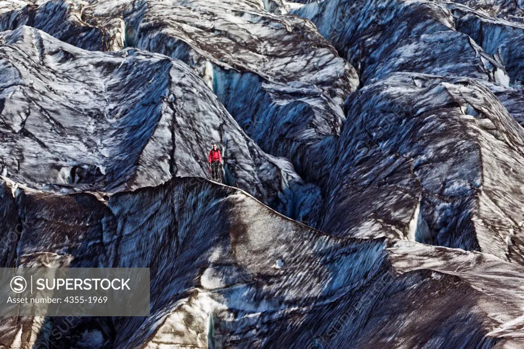 A hiker in dressed in red stands out on the ash-blackened Vatnajokull Glacier, Iceland