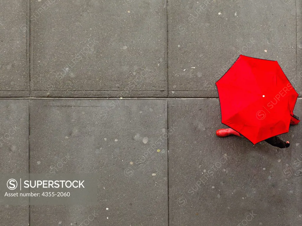A person beneath a red umbrella strides along the sidewalk in New York city.