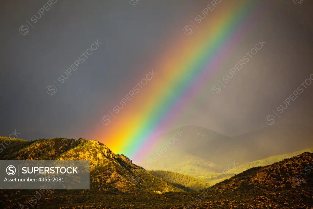 An enormous rainbow emanating from behind a sunlit mountain.