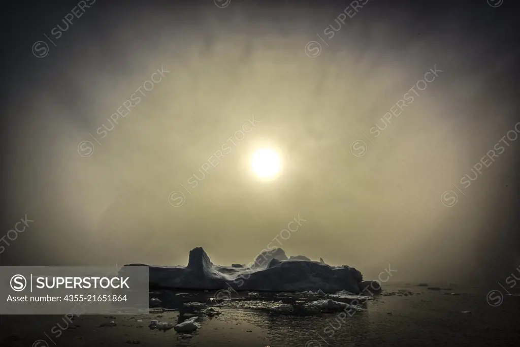 An iceberg emerges as the sun penetrates the fog in Blackhead, Antarctica.