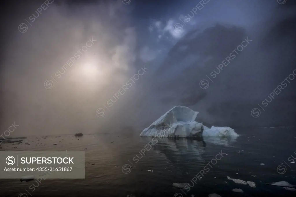 Sun rises through heavy fog showing large icebergs in Blackhead, Antarctica