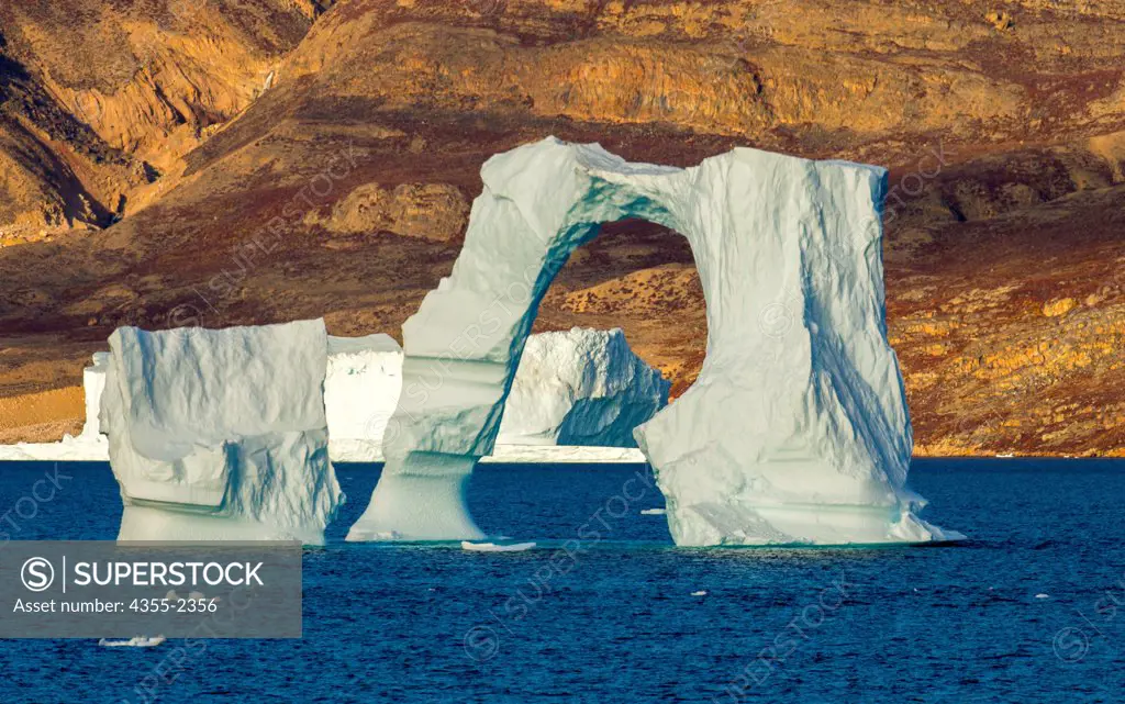 Greenland, Arched iceberg against rocky shore