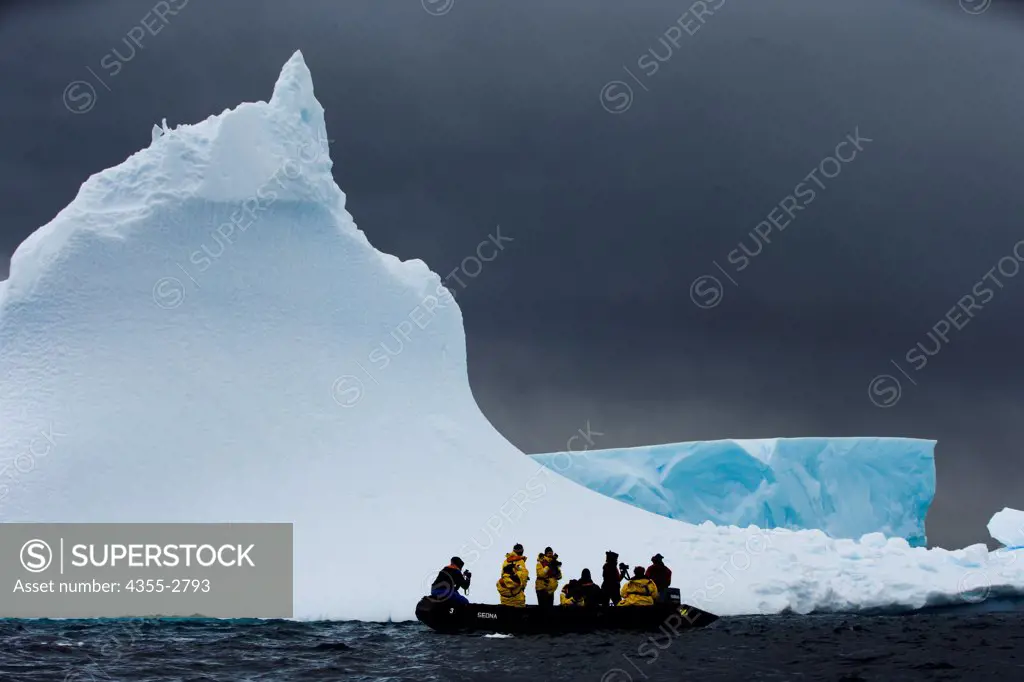 Tourists on boat in front a massive iceberg on Petermann Island, Antarctica